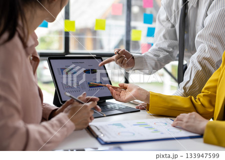 Professionals engaged in a business meeting, analyzing charts and graphs on a laptop, brainstorming session in office. 133947599