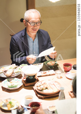 旅館の夕食でシニア夫婦がメニュー表を見ながら団らんを楽しむひととき 133948658