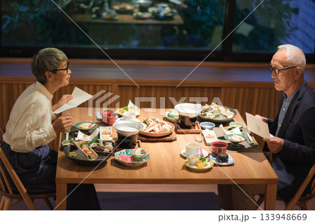旅館の夕食でシニア夫婦がメニュー表を見ながら団らんを楽しむひととき 133948669