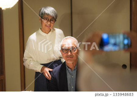 家族旅行の夕食で娘に還暦祝いの記念写真を撮ってもらうシニア夫婦 133948683