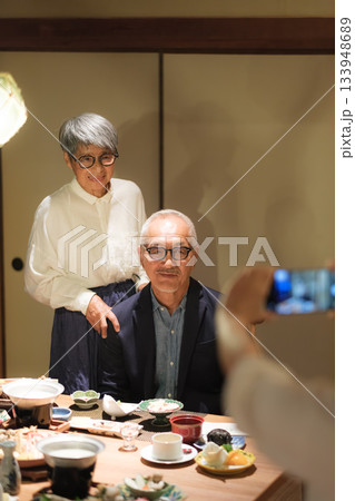 家族旅行の夕食で娘に還暦祝いの記念写真を撮ってもらうシニア夫婦 家族旅行の夕食で娘に還暦祝いの記念写真を撮ってもらうシニア夫婦 133948689