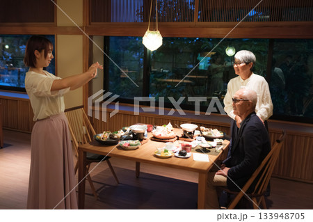 家族旅行の夕食で娘に還暦祝いの記念写真を撮ってもらうシニア夫婦 家族旅行の夕食で娘に還暦祝いの記念写真を撮ってもらうシニア夫婦 133948705