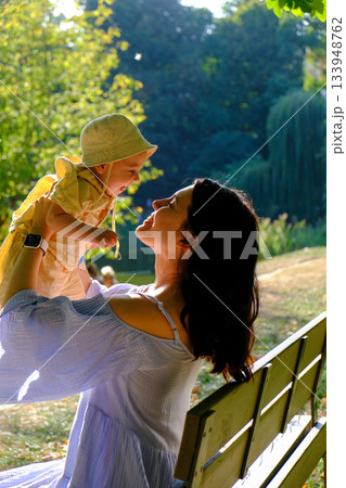 Mother Lifting Baby Outdoors in Sunny Park Mother Lifting Baby Outdoors in Sunny Park 133948762