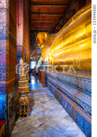 Golden reclining Buddha statue inside Wat Pho temple in Bangkok, Thailand, captured in a grand perspective showing its monumental scale and serene spiritual atmosphere. 133948880