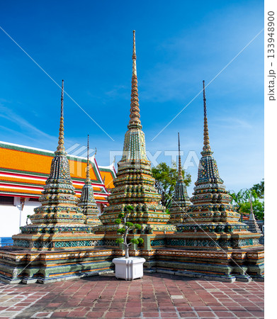 Exterior view of Wat Pho with richly decorated stupas covered in colorful floral ceramics and golden temple roofs shining under a clear blue sky on a bright sunny day in Bangkok. Exterior view of Wat Pho with richly decorated stupas covered in colorful floral ceramics and golden temple roofs shining under a clear blue sky on a bright sunny day in Bangkok. 133948900