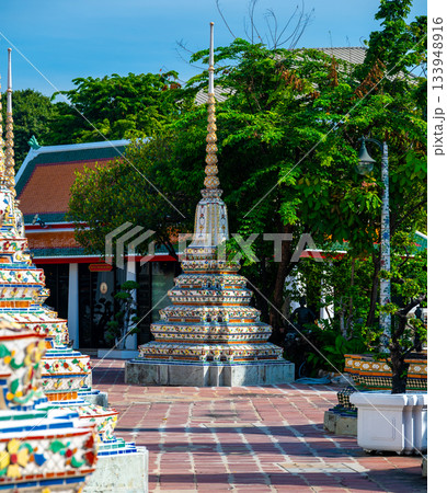 Exterior view of Wat Pho with richly decorated stupas covered in colorful floral ceramics and golden temple roofs shining under a clear blue sky on a bright sunny day in Bangkok. Exterior view of Wat Pho with richly decorated stupas covered in colorful floral ceramics and golden temple roofs shining under a clear blue sky on a bright sunny day in Bangkok. 133948916
