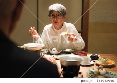 シニア夫婦が還暦祝いの旅行で旅館の会席料理をゆったり味わう夕食シーン 133948940