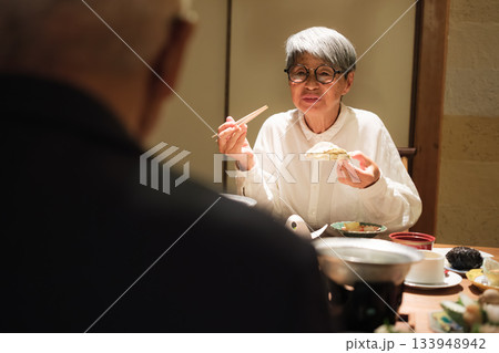 シニア夫婦が還暦祝いの旅行で旅館の会席料理をゆったり味わう夕食シーン 133948942