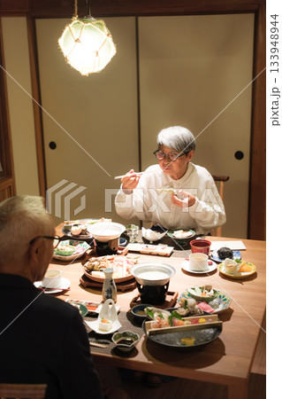 シニア夫婦が還暦祝いの旅行で旅館の会席料理をゆったり味わう夕食シーン 133948944