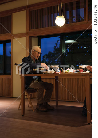 シニア夫婦が還暦祝いの旅行で旅館の会席料理をゆったり味わう夕食シーン 133948946