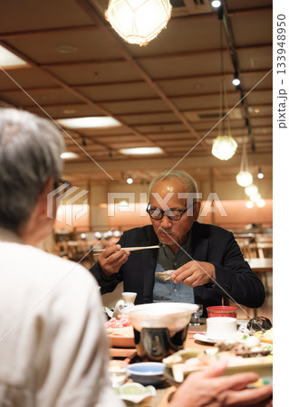 シニア夫婦が還暦祝いの旅行で旅館の会席料理をゆったり味わう夕食シーン シニア夫婦が還暦祝いの旅行で旅館の会席料理をゆったり味わう夕食シーン 133948950