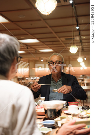 シニア夫婦が還暦祝いの旅行で旅館の会席料理をゆったり味わう夕食シーン シニア夫婦が還暦祝いの旅行で旅館の会席料理をゆったり味わう夕食シーン 133948951