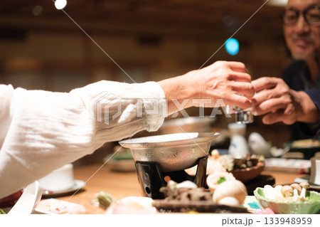 シニア夫婦が還暦祝いの旅行で旅館の会席料理をゆったり味わう夕食シーン シニア夫婦が還暦祝いの旅行で旅館の会席料理をゆったり味わう夕食シーン 133948959