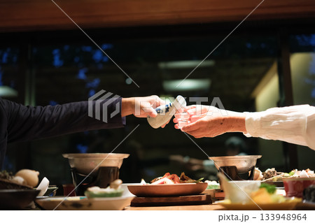 シニア夫婦が還暦祝いの旅行で旅館の会席料理をゆったり味わう夕食シーン 133948964