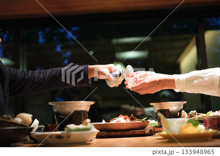 シニア夫婦が還暦祝いの旅行で旅館の会席料理をゆったり味わう夕食シーン 133948965