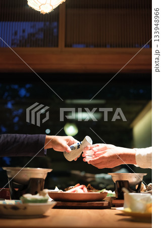 シニア夫婦が還暦祝いの旅行で旅館の会席料理をゆったり味わう夕食シーン 133948966