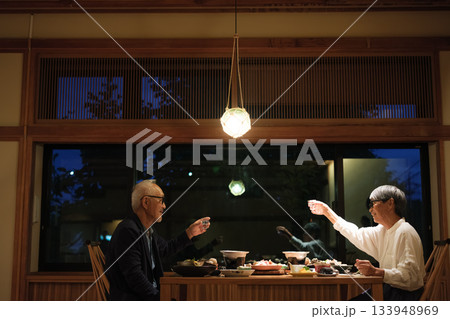 シニア夫婦が還暦祝いの旅行で旅館の会席料理をゆったり味わう夕食シーン 133948969