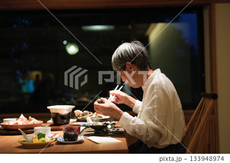 シニア夫婦が還暦祝いの旅行で旅館の会席料理をゆったり味わう夕食シーン 133948974