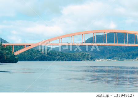 山あいの町に広がる静かな漁港風景。穏やかな水面に並ぶ漁船とローカルな町並み 133949127