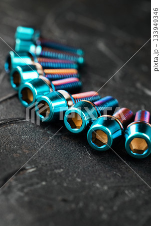 A row of blue Titanium bicycle screws on a black textured background with free space A row of blue Titanium bicycle screws on a black textured background with free space 133949346