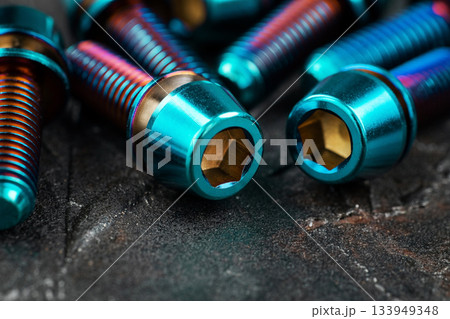 Blue titanium screws in a row with a hexagon head on a black textured background close-up 133949348