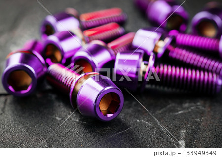 A series of titanium pink hexagon head screws on a black textured background close-up 133949349
