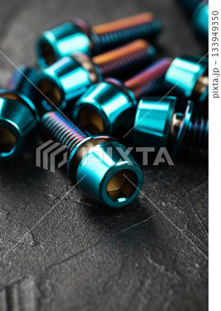 Blue titanium screws in a row with a hexagon head on a black textured background close-up 133949350