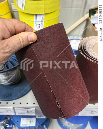 Hand holding sandpaper roll in hardware store aisle for DIY projects Hand holding sandpaper roll in hardware store aisle for DIY projects 133949551