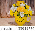 Yellow smiley mug with fresh flower bouquet on wooden background Yellow smiley mug with fresh flower bouquet on wooden background 133949759