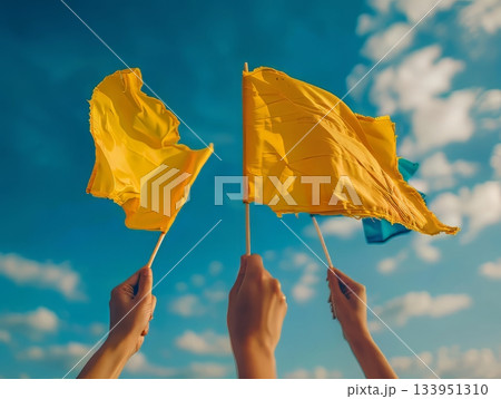 Hands raising yellow flags against blue sky 133951310