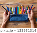 Pencil case with hands on wooden desk 133951314