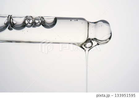 Clear cosmetic pipette dispensing serum drop against white background Clear cosmetic pipette dispensing serum drop against white background 133951595