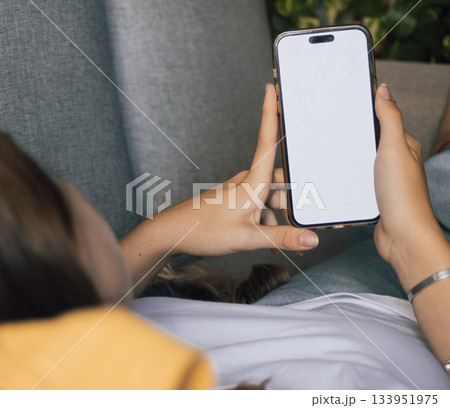 Close up of a young woman holding smartphone with blank screen while relaxing on sofa at home. Ideal for digital resources, e commerce, and mobile app 133951975