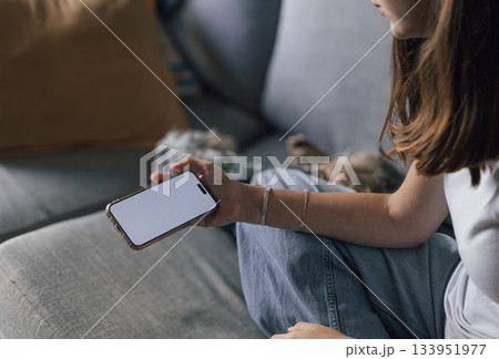 Young woman on a sofa using a smartphone with blank screen,casually shopping or studying online from home Concept of relaxed, modern lifestyle vibe 133951977