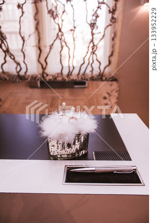 Wedding rings resting on feathers with pen on desk 133952229