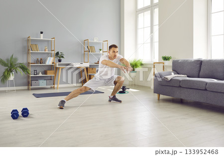 Fit young man doing side lunge stretching exercises during sports workout at home 133952468