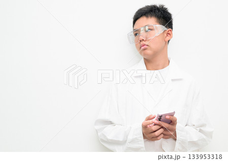 Young Asian Boy Dressed as Scientist with Lab Coat Using Mobile Phone and Thinking Young Asian Boy Dressed as Scientist with Lab Coat Using Mobile Phone and Thinking 133953318