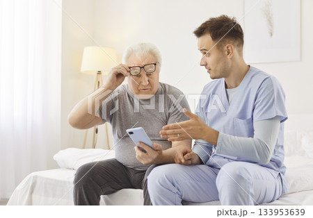 Young cheerful male nurse showing elderly man how to use smartphone in clinic 133953639