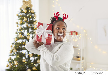 Joyful African American woman holding red gift box and celebrating Christmas in decorated room. 133953640