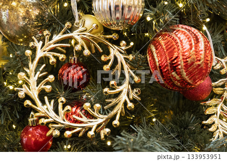 Golden wreath with red ornaments on Christmas tree creating rich festive classic holiday decor. Golden wreath with red ornaments on Christmas tree creating rich festive classic holiday decor. 133953951