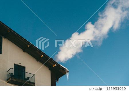 Smoke rising from a roof in winter with icicles hanging and a clear blue sky in view 133953960