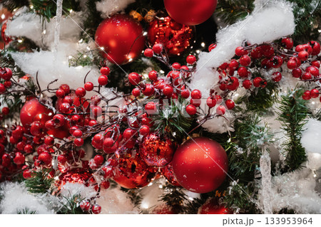 Red berries and ornaments on snowy Christmas tree with warm lights and festive classic holiday decor. Red berries and ornaments on snowy Christmas tree with warm lights and festive classic holiday decor. 133953964