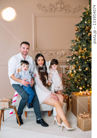 Family celebration in a cozy room with a decorated Christmas tree, gifts, and joyful laughter during winter holidays Family celebration in a cozy room with a decorated Christmas tree, gifts, and joyful laughter during winter holidays 133954074