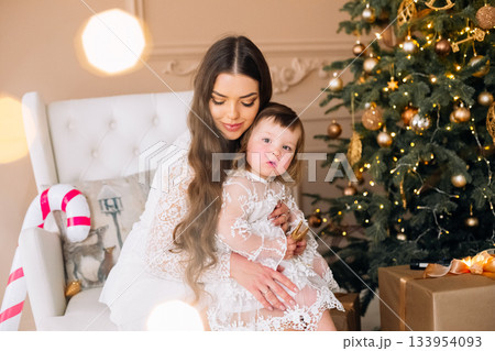 Mother and child share a cozy moment by decorated Christmas tree in warm living room setting during holiday season Mother and child share a cozy moment by decorated Christmas tree in warm living room setting during holiday season 133954093