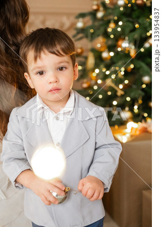 Child holding a glowing light in a cozy living room decorated for the holidays while standing near a Christmas tree with twinkling lights Child holding a glowing light in a cozy living room decorated for the holidays while standing near a Christmas tree with twinkling lights 133954837