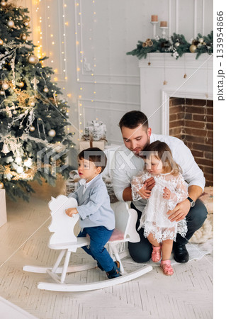Children enjoy holiday spirit while playing with a rocking horse near a festive Christmas tree and warm fireplace in a cozy home setting during winter 133954866