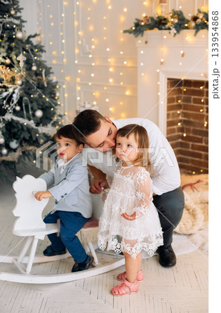 Family moment with children by the Christmas tree enjoying the festive decorations during the holiday season indoors 133954868