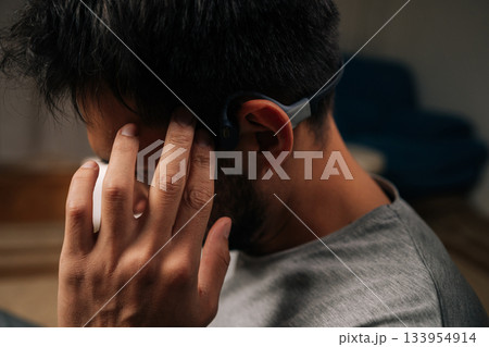 Close-up of man wearing bone conduction headphones, listening to audio content, interacting with device by touching temple, demonstrating modern wireless technology and convenient listening lifestyle. Close-up of man wearing bone conduction headphones, listening to audio content, interacting with device by touching temple, demonstrating modern wireless technology and convenient listening lifestyle. 133954914