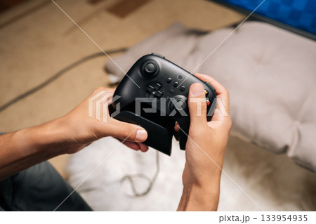 Close-up of unrecognizable person holding modern black wireless game controller in focused home gaming session, hands on buttons and joysticks, enjoying casual digital entertainment, competitive play. 133954935