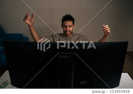 Cheerful young man reacting with excitement and joy, raising arms in celebration watching live broadcast on television, celebrating victory, cheering for favorable outcome, success at home. Cheerful young man reacting with excitement and joy, raising arms in celebration watching live broadcast on television, celebrating victory, cheering for favorable outcome, success at home. 133954938
